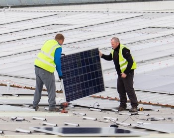 Dos hombres sostienen un panel solar en el tejado